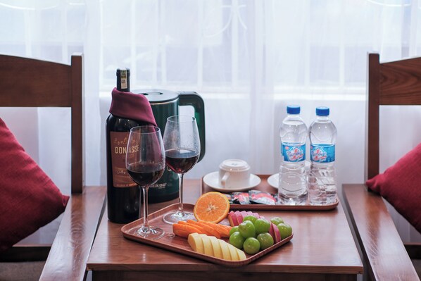 A wooden table with a bottle of wine, glasses, water bottles, and a tray of fruit.