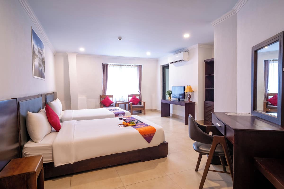 Una habitación de hotel con dos camas, un escritorio, una silla y un televisor.