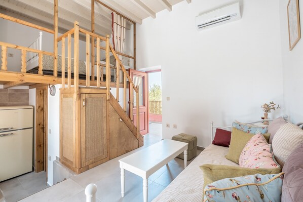 A room with a wooden staircase, a white sofa, a small table, and a kitchenette.
