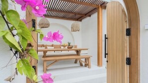 Eine Terrasse im Freien mit einem Holztisch und -bänken, einer hängenden Lampe und einer Holztür.
