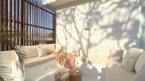 Ein sonniger Außenbereich mit Sitzgelegenheiten, einer Couch, einem kleinen Tisch mit Getränken und einer Flasche.
