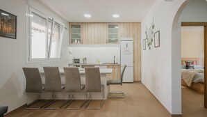 Una cucina moderna con mobili bianchi, un'area pranzo con quattro sedie e un frigorifero a vista.