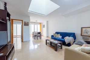 A living room with a blue sofa, a coffee table, a TV, and a dining area with chairs and a table.