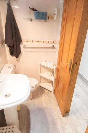 Une salle de bain équipée de toilettes, d’un lavabo et d’étagères où sont rangés les articles de toilette.