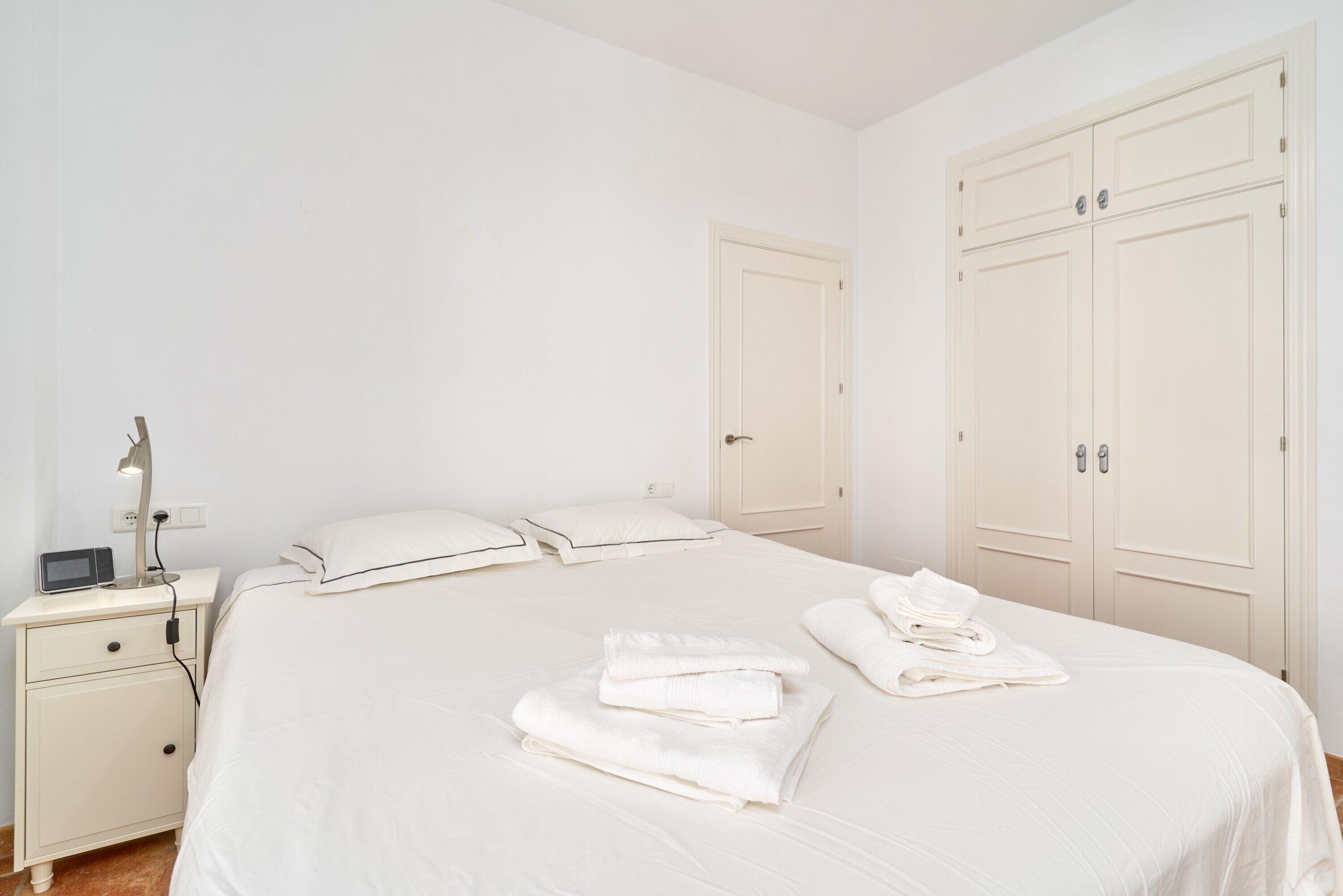 Un dormitorio con cama, mesita de noche, lámpara y armario.