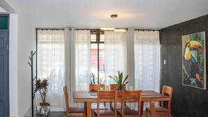 A dining area with a wooden table and chairs, a potted plant, and a painting on the wall.