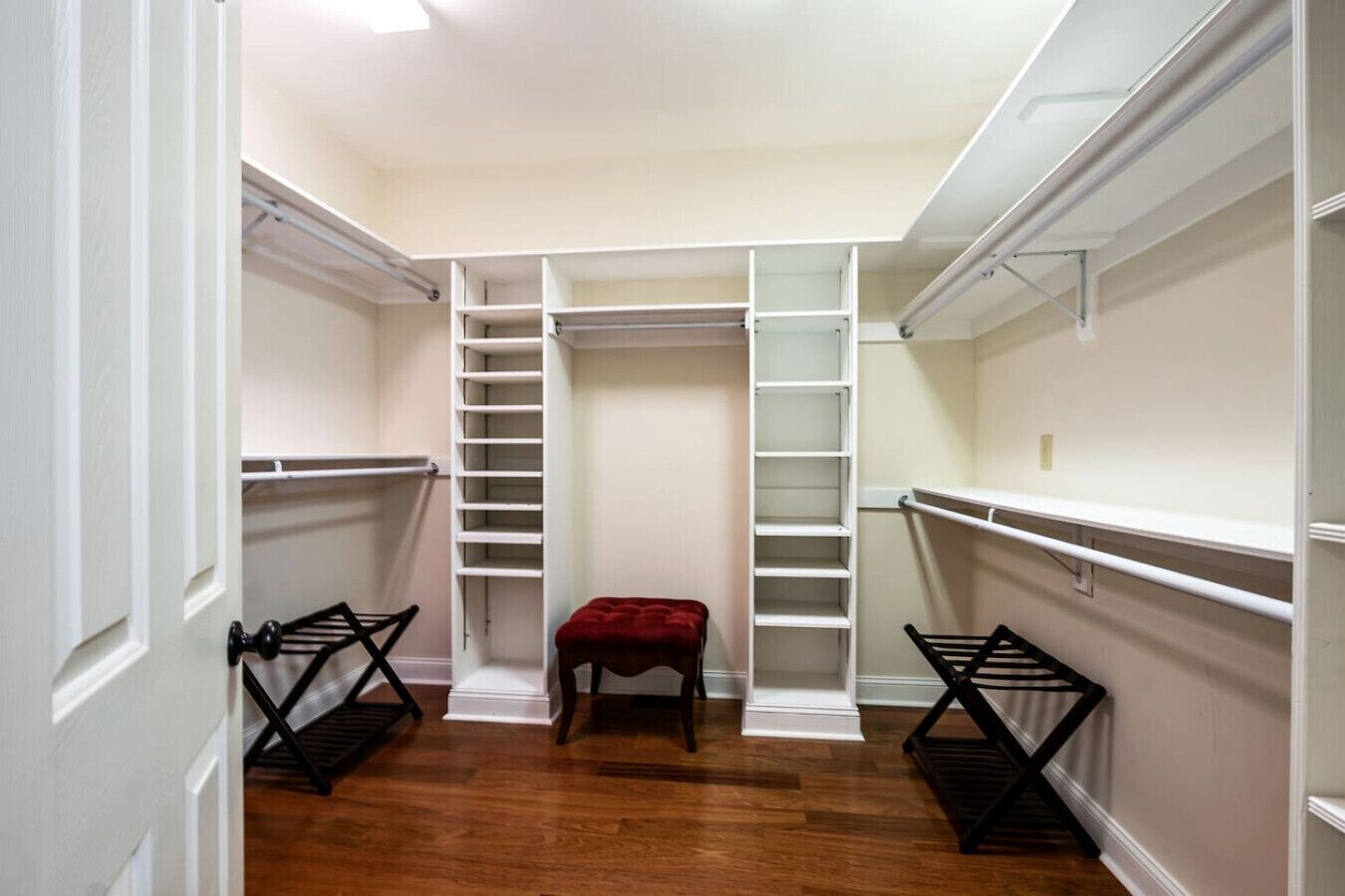 Ein begehbarer Kleiderschrank mit offenen Regalen, einem roten Hocker und schwarzen Wäscheständern.