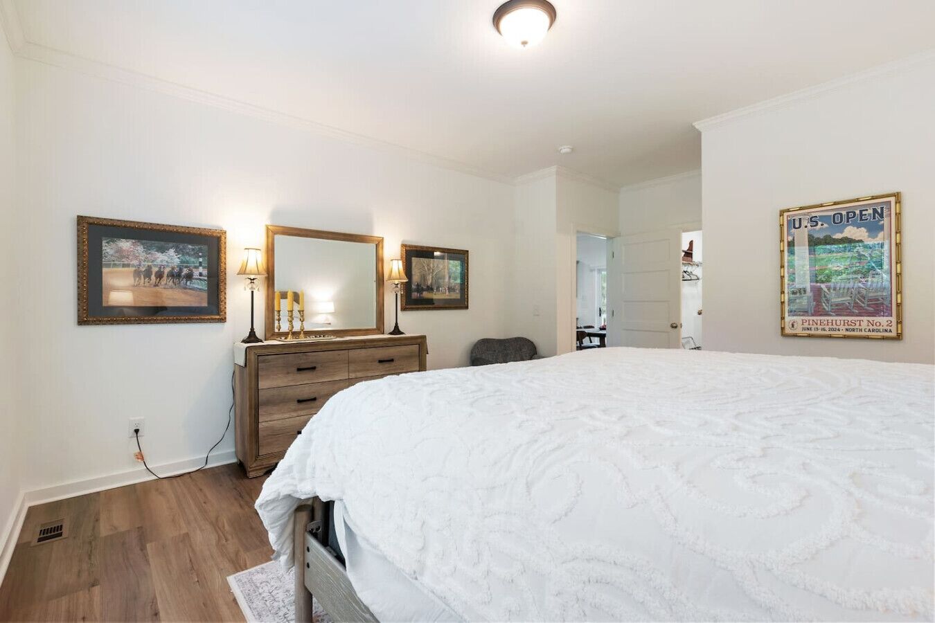 A bedroom with a large bed, a dresser, a mirror, and a framed picture on the wall.