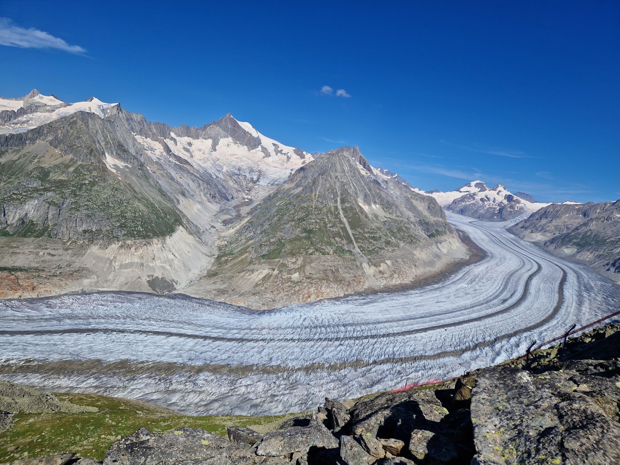 Un glacier dont le tracé sinueux serpente au milieu de montagnes escarpées, sous un ciel d’un bleu limpide.