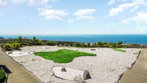 Un jardin aménagé avec un sentier de galets, des pelouses verdoyantes et une vue sur l’océan.