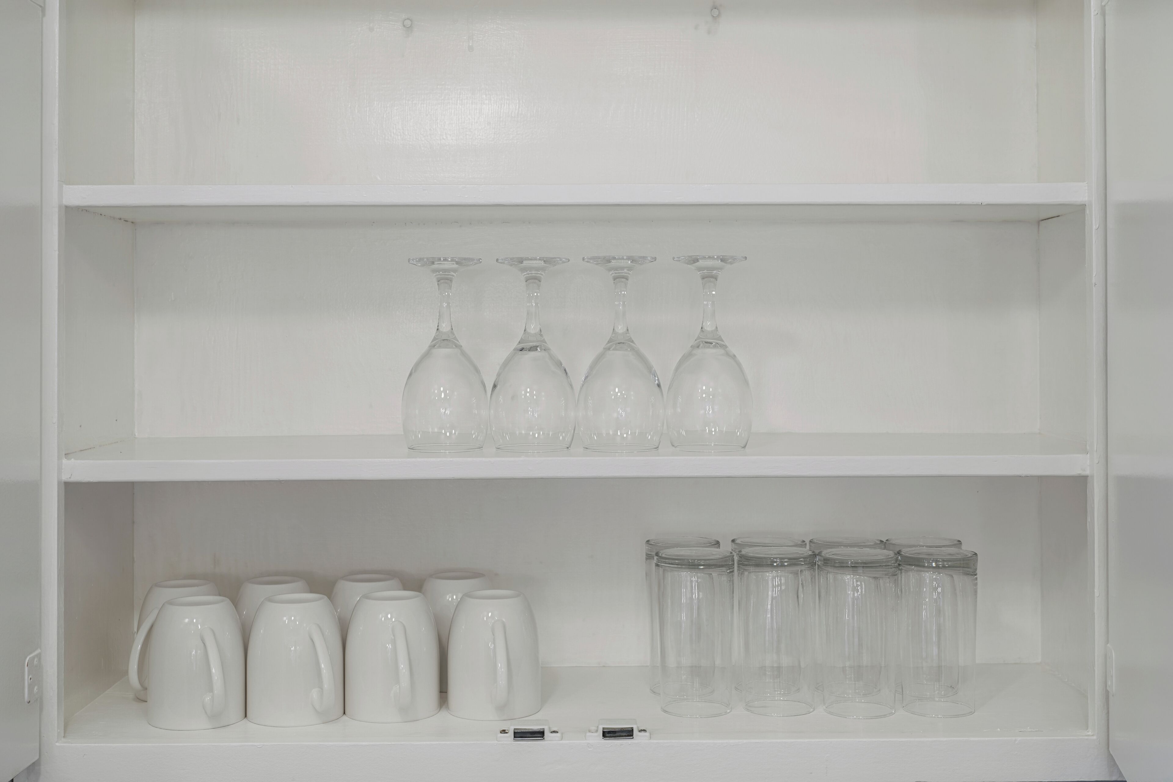 A white shelf with wine glasses and mugs.