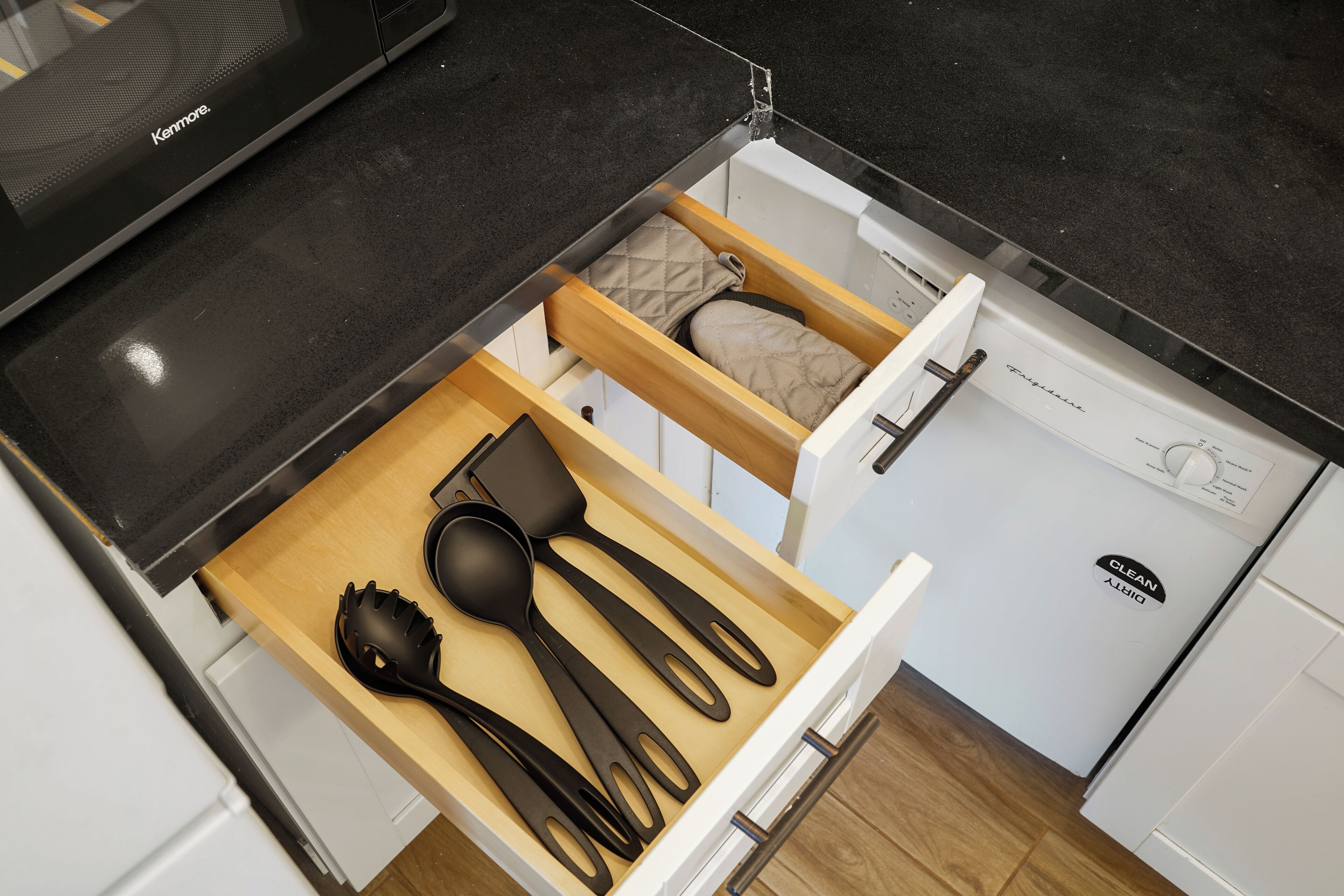 A kitchen drawer with black kitchen utensils, a white refrigerator, and a Kenmore appliance.