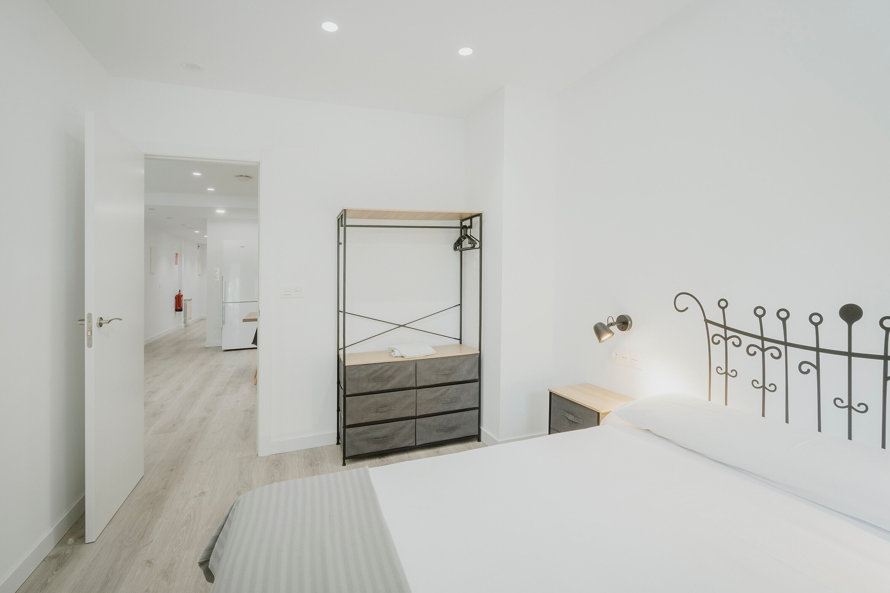 Un dormitorio con una cama, un armario, una mesita de noche y una lámpara de pared.