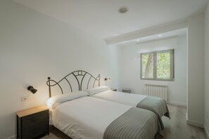 Ein Schlafzimmer mit zwei Betten, einem Nachttisch, einer Wandleuchte, einem Fenster mit Blick auf Grünflächen und einer Heizung.