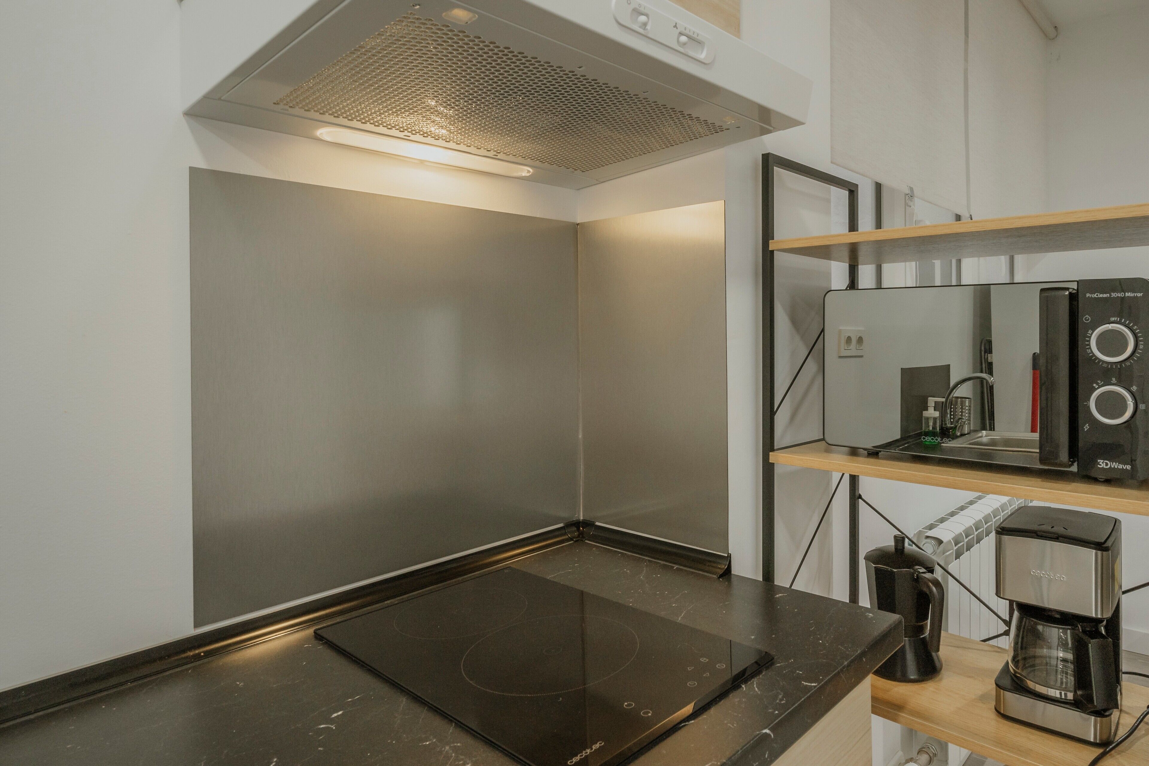 Una cocina moderna con una placa de inducción integrada, una cafetera y un espejo con forma de ola tridimensional.