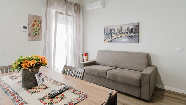En stue med en sofa, et spisebord med en vase blomster, et billede på væggen og en brandslukker.