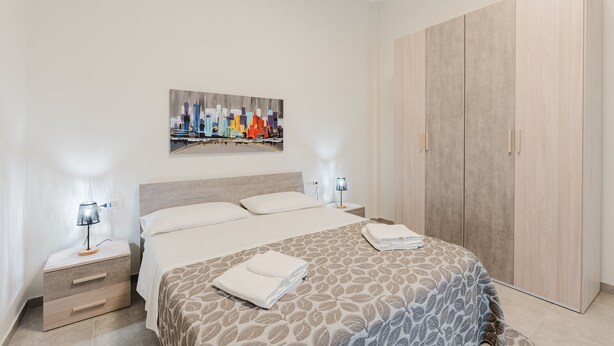 A hotel room with a bed, nightstands, a wardrobe, and a cityscape painting on the wall.