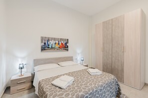 Ett hotellrum med en säng, sängbord, en garderob och en tavla med en stadsbild på väggen.