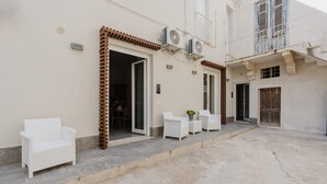 A building with a covered patio, white wicker furniture, and air conditioning units.