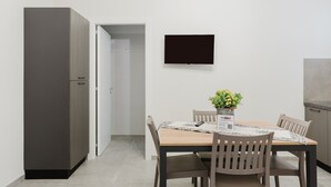 A modern kitchen with a built-in oven, a dining table with four chairs, and a flat-screen TV mounted on the wall.