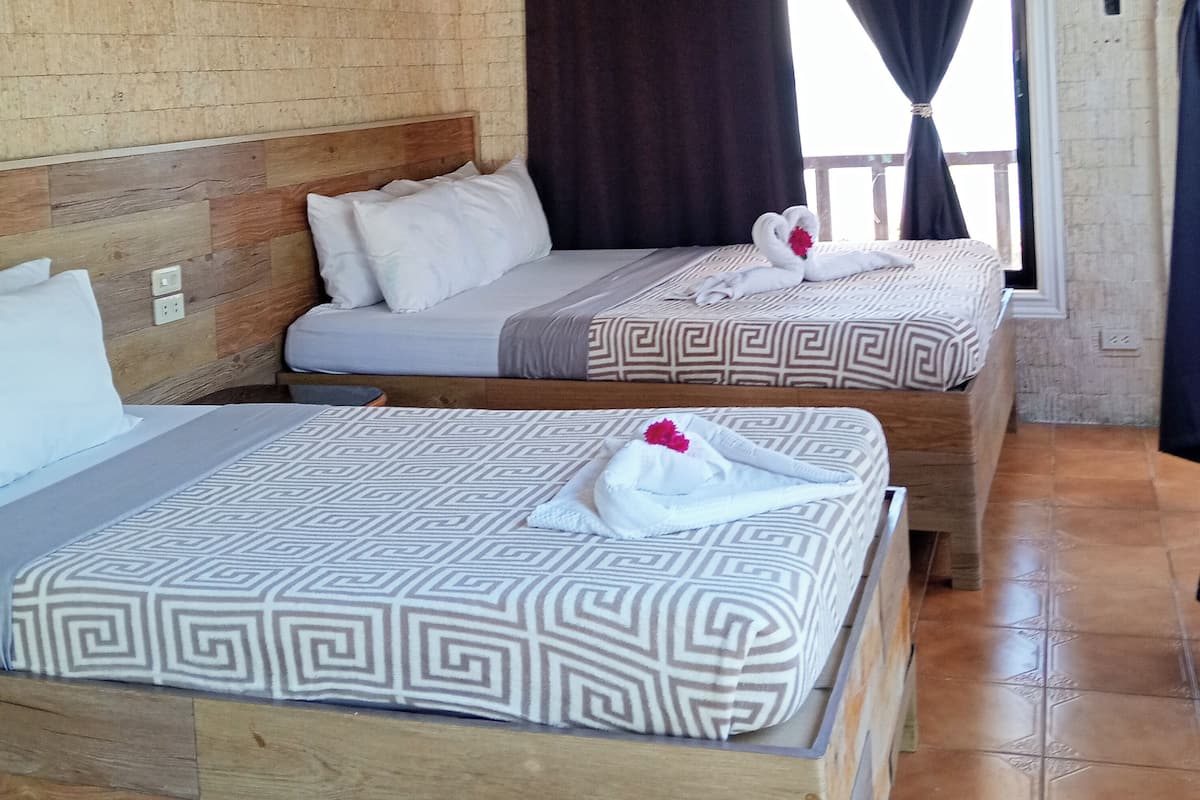 Two beds with patterned bedding, a wooden headboard, and a window with curtains.