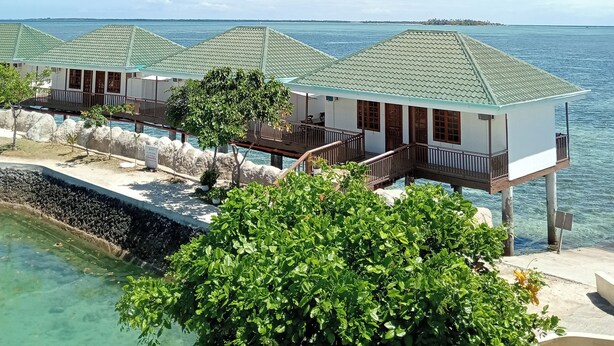 Een rij overwaterbungalows met helder uitzicht op de oceaan, verbonden door een brug, en met een zwembad.