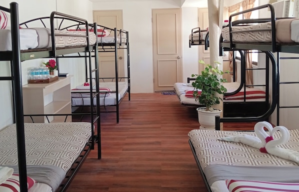 Une chambre de dortoir avec des lits superposés, un plancher en bois, une plante en pot et une décoration en forme de cœur faite avec une serviette.