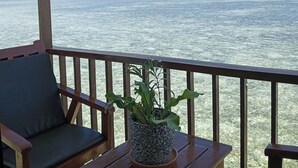 Een houten terras met een bloempot en een stoel, met uitzicht op een waterpartij met land en gebouwen in de verte.