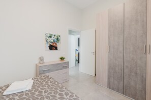 A bedroom with a bed, a dresser, a wardrobe, a painting, and a door leading to another room. - Apartment 'Lazzara 19 - Home 01' with Balcony, Wi-Fi and Air Conditioning (Marsala)