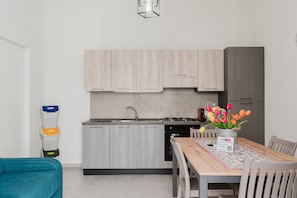 A modern kitchen with light wood cabinets, a stainless steel sink, and a dining area with a wooden table and chairs. - Apartment 'Lazzara 19 - Home 01' with Balcony, Wi-Fi and Air Conditioning (Marsala)