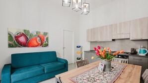 A modern kitchen with light wood cabinets, a teal sofa, and a dining table with a patterned runner. - Apartment 'Lazzara 19 - Home 01' with Balcony, Wi-Fi and Air Conditioning (Marsala)