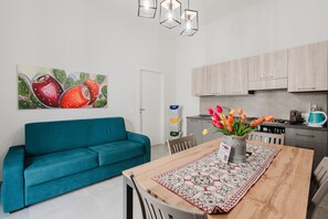 A modern kitchen with light wood cabinets, a teal sofa, and a dining table with a patterned runner.