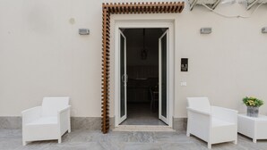 A building entrance with a wooden pergola, two white wicker chairs, and a potted plant. - Apartment 'Lazzara 19 - Home 01' with Balcony, Wi-Fi and Air Conditioning (Marsala)