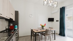 A modern kitchen with a stove, cabinets, and a dining area with chairs and a table. - Apartment 'Lazzara 19 - Home 01' with Balcony, Wi-Fi and Air Conditioning (Marsala)