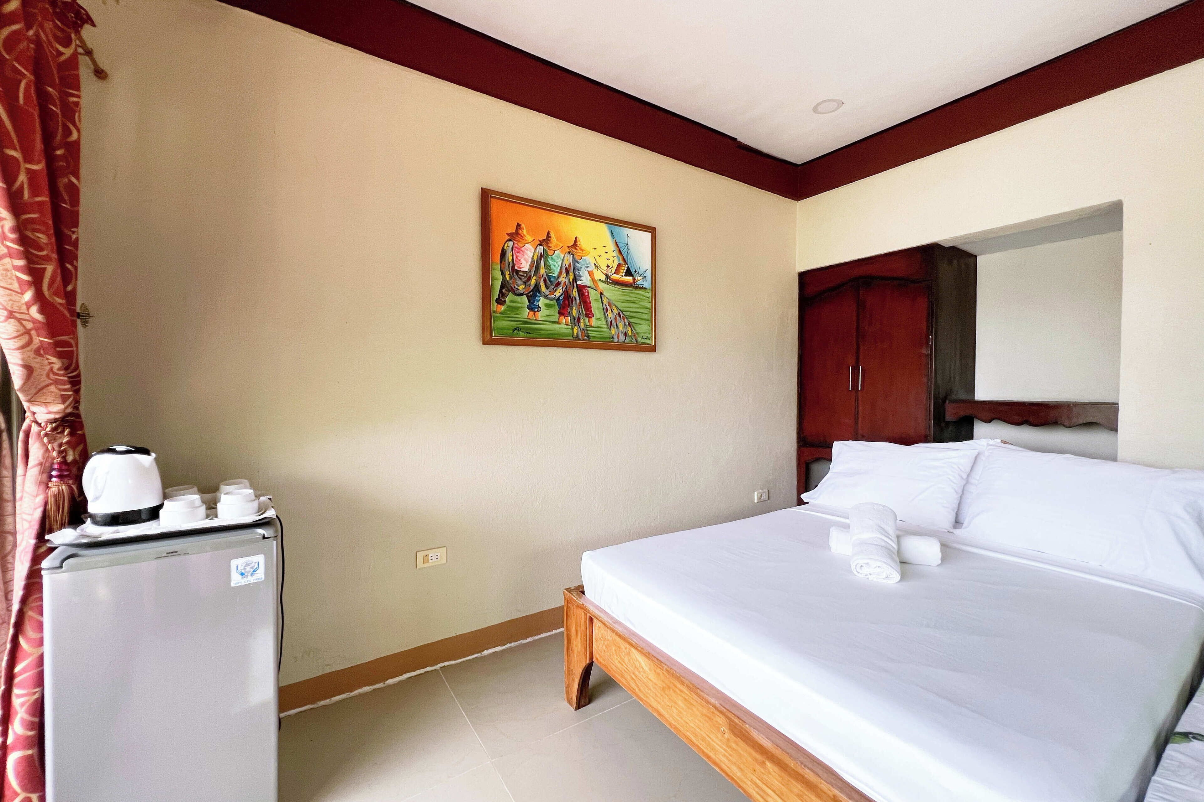 Una habitación de hotel con una cama, un refrigerador pequeño, un cuadro en la pared y un armario de madera.