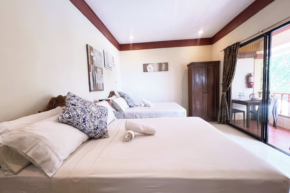 Ein Hotelzimmer mit zwei Betten, einem Holzschrank und einem Balkon mit Tisch und Stühlen.
