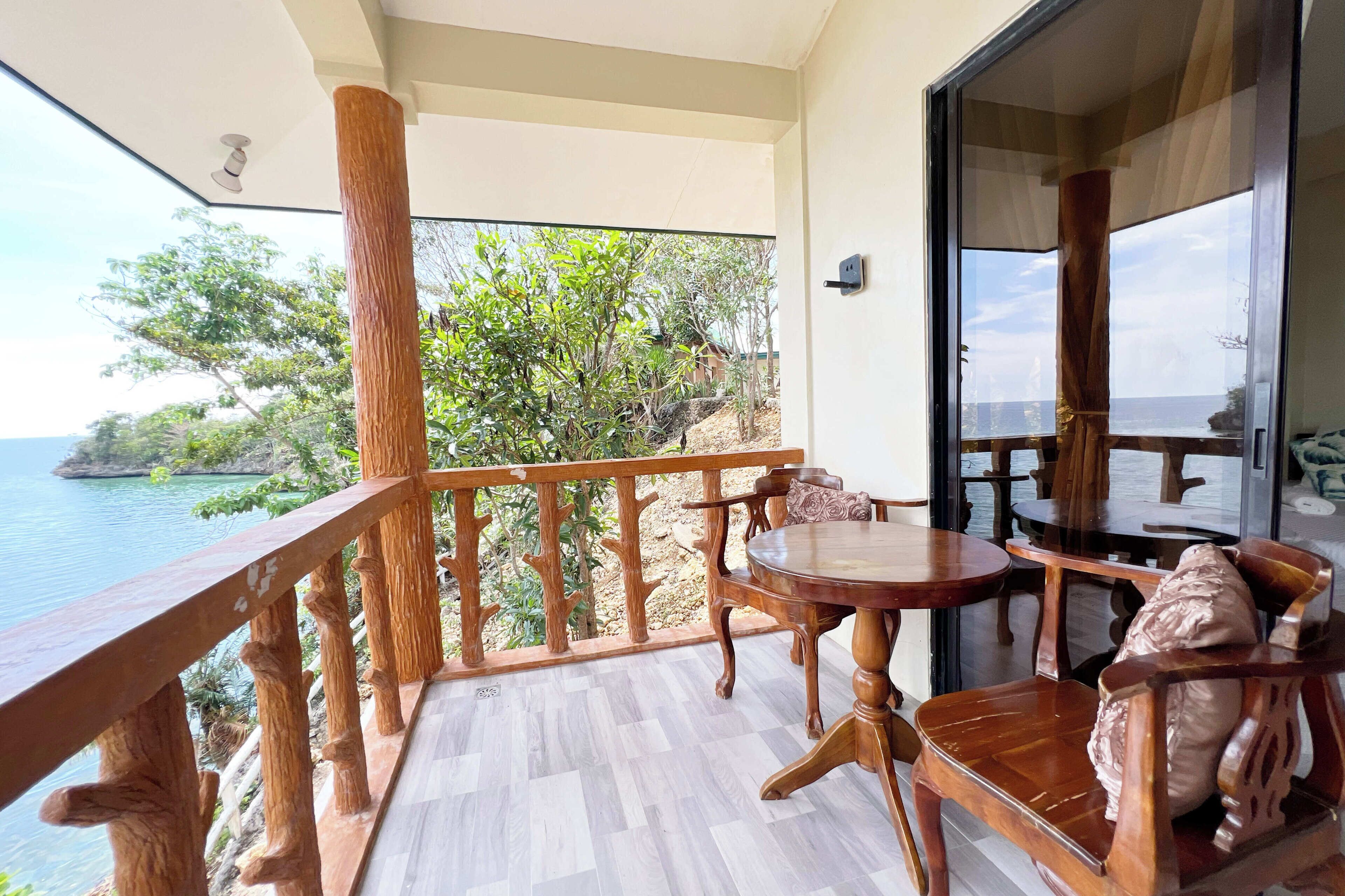 A balcony with wooden railings, a round wooden table, and two wooden chairs with cushions.
