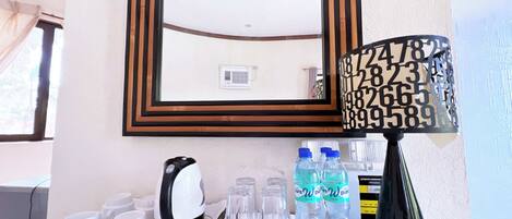 Une chambre d’hôtel équipée d’une machine à café, de tasses, de verres et de bouteilles d’eau sur le comptoir.