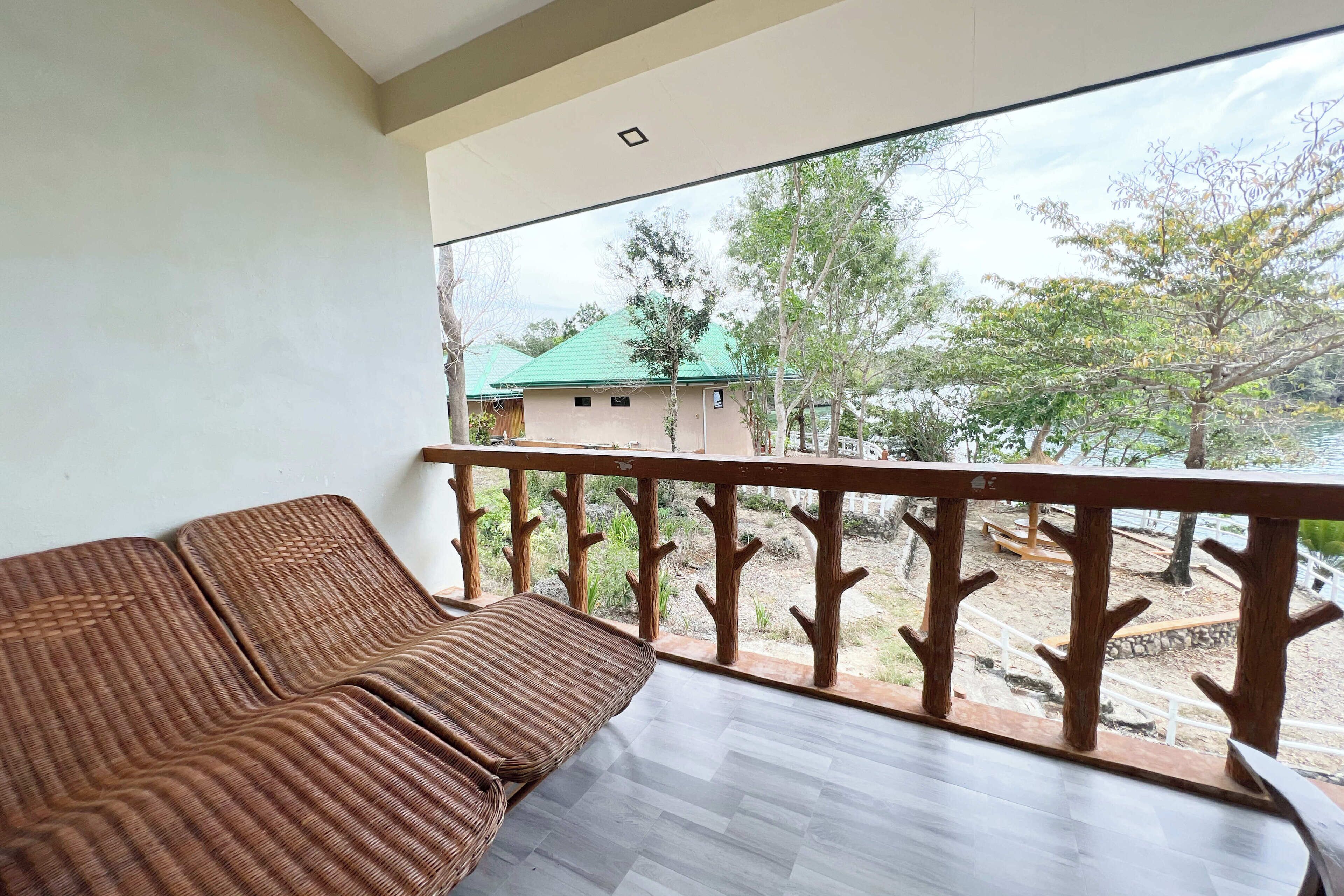 A balcony with a wicker sofa, a wooden railing, and a view of a building with a green roof.