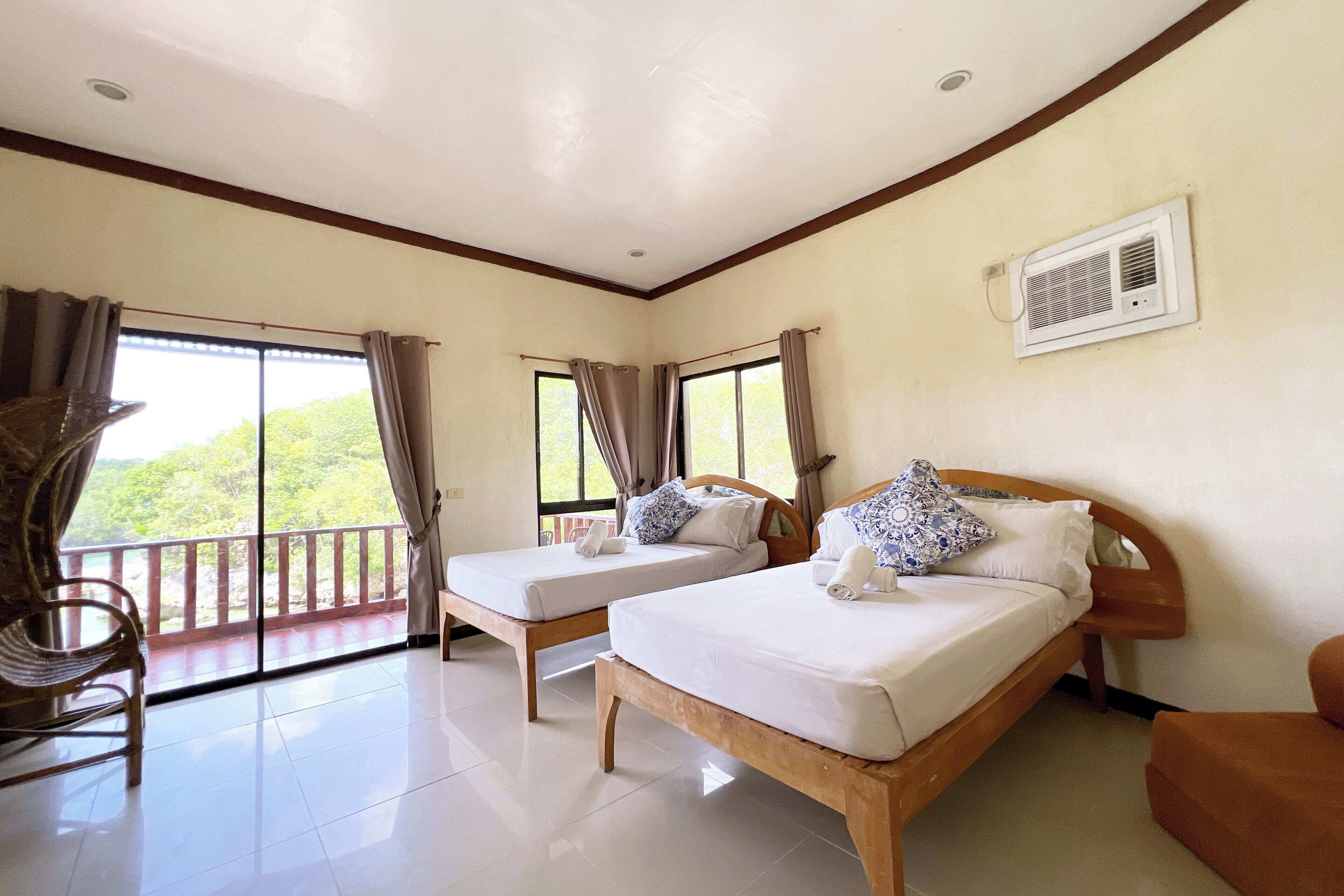 A hotel room with two beds, a balcony, and a ceiling fan.