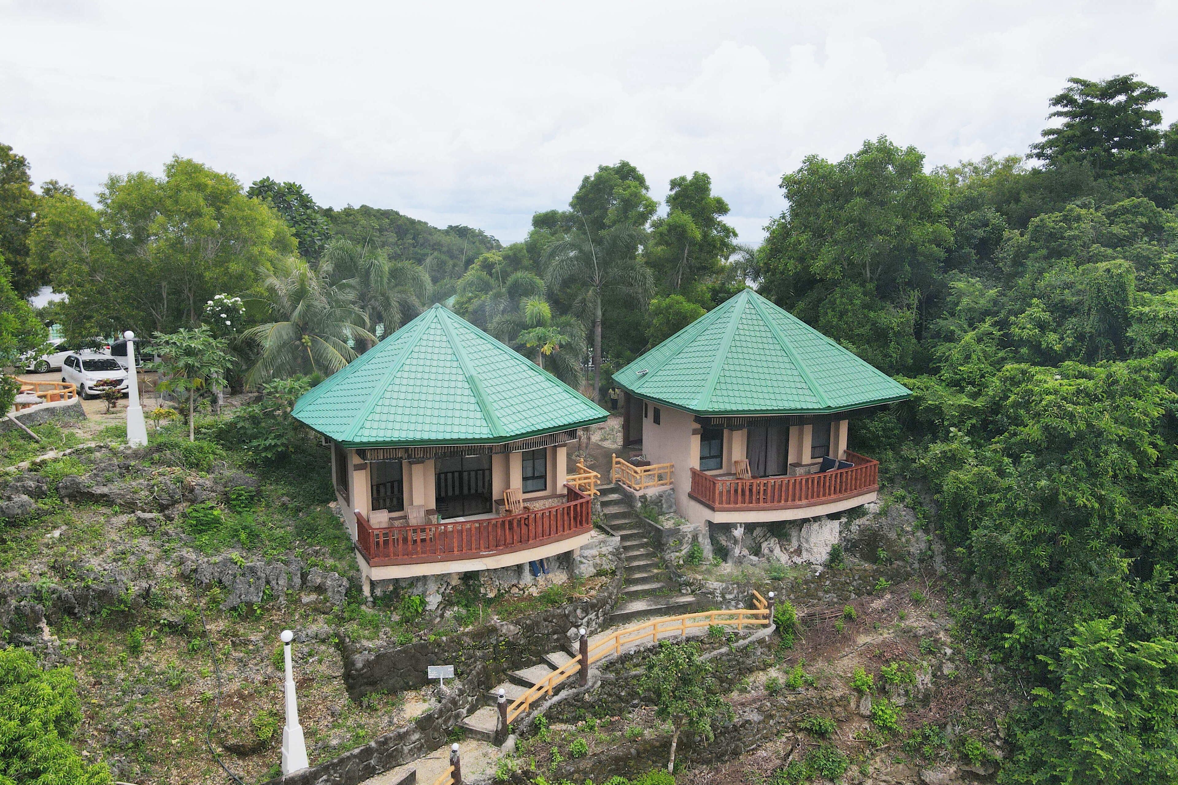 Two green-roofed buildings with balconies, situated on a rocky hillside surrounded by dense greenery.