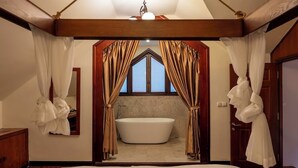 Une chambre avec un grand lit, une fenêtre avec des rideaux, une baignoire et un plafond en bois.
