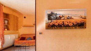 Een kamer met een bed, een schilderij van een zonnebloemenveld, een radiator en een plank met spullen.