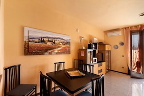 Un comedor con mesa, sillas, un cuadro y una cocina con armarios y aire acondicionado.