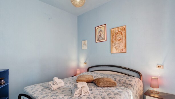 Een slaapkamer met een bed, kussens, een nachtkastje met een lamp en kunst aan de muur.