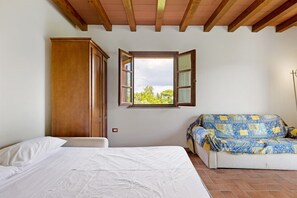 A bedroom with a bed, a sofa, a wardrobe, and a window with an open view.