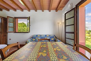A room with a bed, a table, and a window with a view of greenery.