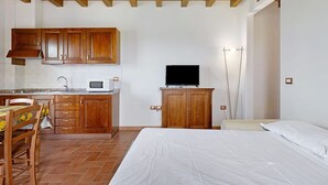 A bedroom with a bed, a TV, wooden cabinets, a kitchen area, and a dining table. - Studio Apartment 'Numero 3' with Shared Garden and Air Conditioning (Montopoli in Val d'Arno)