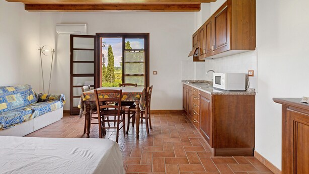 A compact kitchen with wooden cabinets, a dining table with chairs, a sofa, and a bed. - Studio Apartment 'Numero 3' with Shared Garden and Air Conditioning (Montopoli in Val d'Arno)