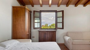 Un dormitorio con una cama, un armario de madera, un ventanal con vistas y un sofá color beige.